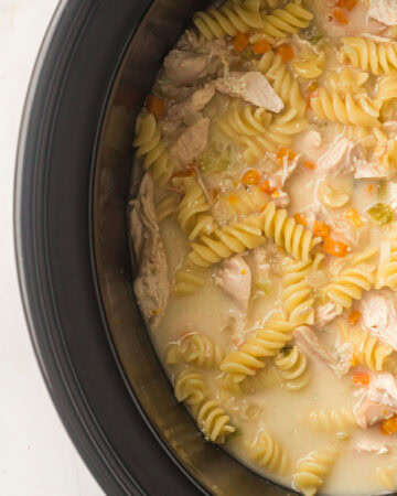 Slow cooker filled with chicken pasta soup with rotini, carrots, and celery.