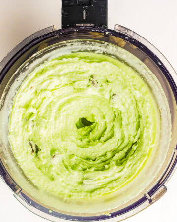Top-down view of pale green ice cream blended smooth inside a food processor bowl.