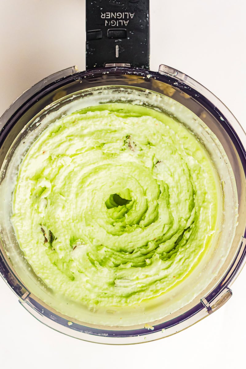Top-down view of pale green ice cream blended smooth inside a food processor bowl.